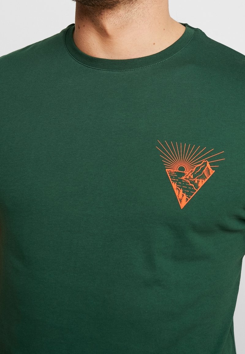 Zelené bavlněné tričko s trojúhelníkovou oranžovou grafikou s krajinou a sluncem, kulatým výstřihem a krátkými rukávy.