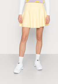 Yellow flared skirt made of soft fabric with an elastic waistband, paired with white sneakers and socks, standing on a neutral background.