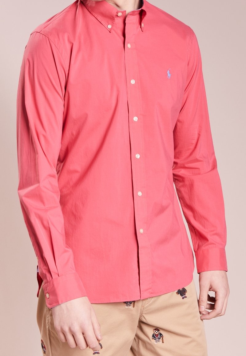 Korálová košile na knoflíky z bavlny, s dlouhými rukávy, klasickým límečkem a malým vyšitým logem na prsou.