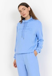 Lichtblauwe sweatshirt met een mouwloze kraag, trekkoorden en de tekst "LAAT NIEUWE AVONTUREN BEGINNEN," gecombineerd met bijpassende lichtblauwe broek.
