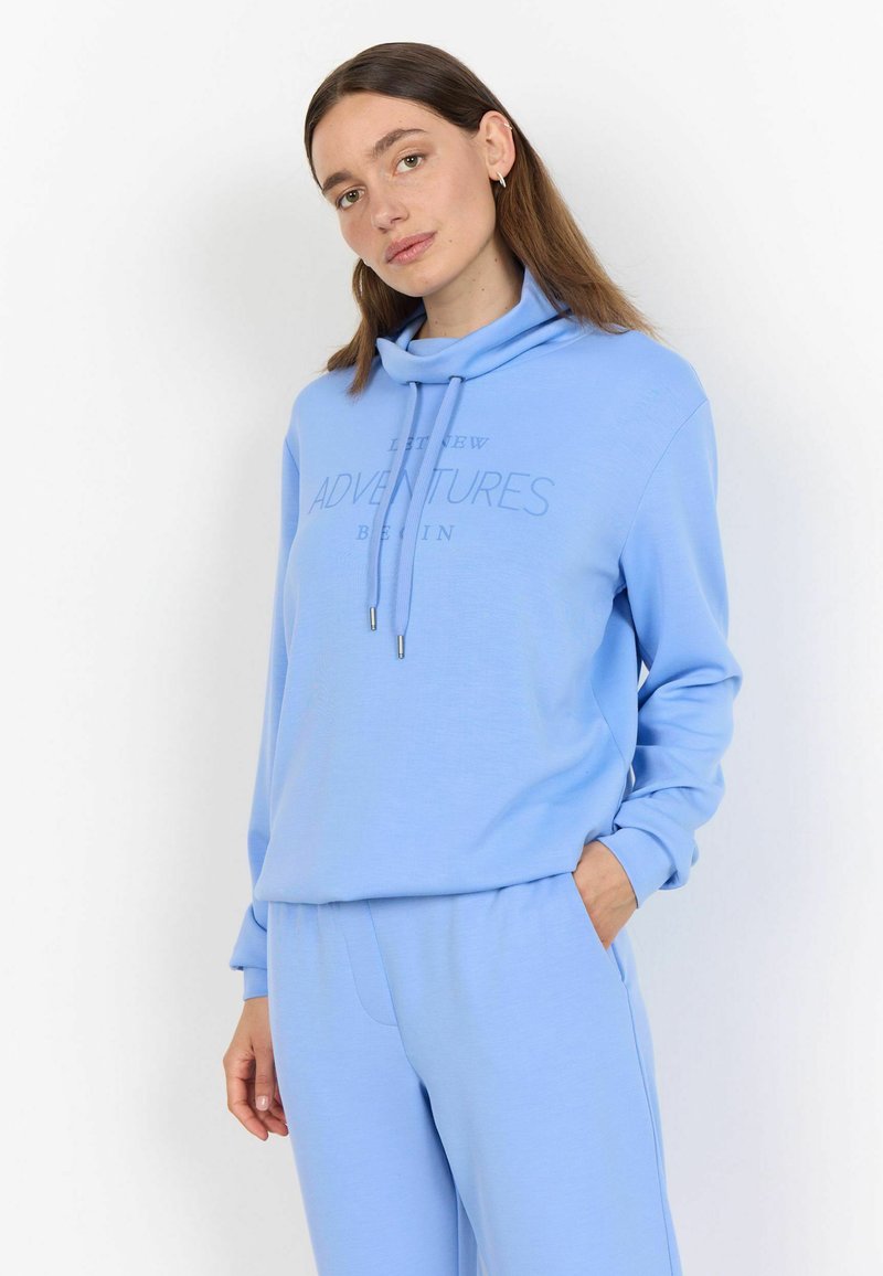 Lichtblauwe sweatshirt met een mouwloze kraag, trekkoorden en de tekst "LAAT NIEUWE AVONTUREN BEGINNEN," gecombineerd met bijpassende lichtblauwe broek.