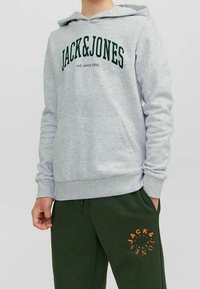 Felpa grigia con cappuccio e logo verde "JACK&JONES", tasca frontale e polsini a costine, abbinata a pantaloni sportivi verdi scuri con stampa arancione.