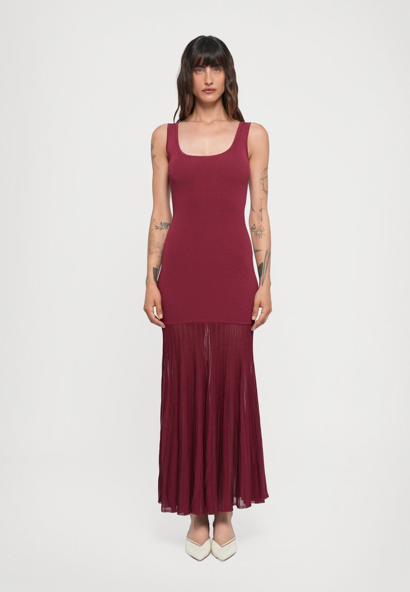 Abito borgogna con top aderente e gonna plissettata, realizzato in tessuto leggero. Presenta un scollo quadrato e una silhouette fluida.