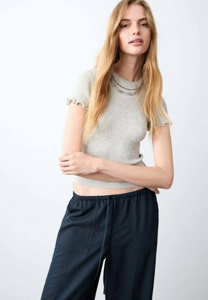 Top gri deschis, scurt, cu dungi și mâneci scurte cu volane, asortat cu pantaloni largi de culoare bleumarin închis, cu talie elastică și buzunare.