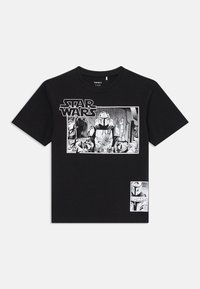 Svart T-skjorte med Star Wars-grafikk som viser en Mandalorian-karakter i rustning, som holder kontroller i cockpiten av et romskip.