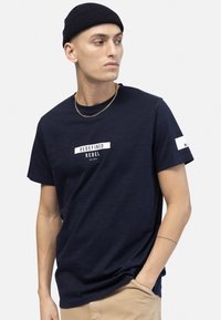Camiseta azul marino hecha de tela suave, con el texto gráfico blanco "REDEFINED REBEL" en el centro y un pequeño acento en la manga.