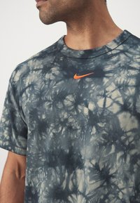 T-shirt en coton tie-dye gris et crème avec un col rond et des manches courtes. Présente un logo Nike orange sur la poitrine.