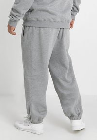 Pantalones de chándal grises con puños elásticos, bolsillos laterales y un corte relajado, hechos de suave tela de algodón. Presentan una textura lisa sin patrones.