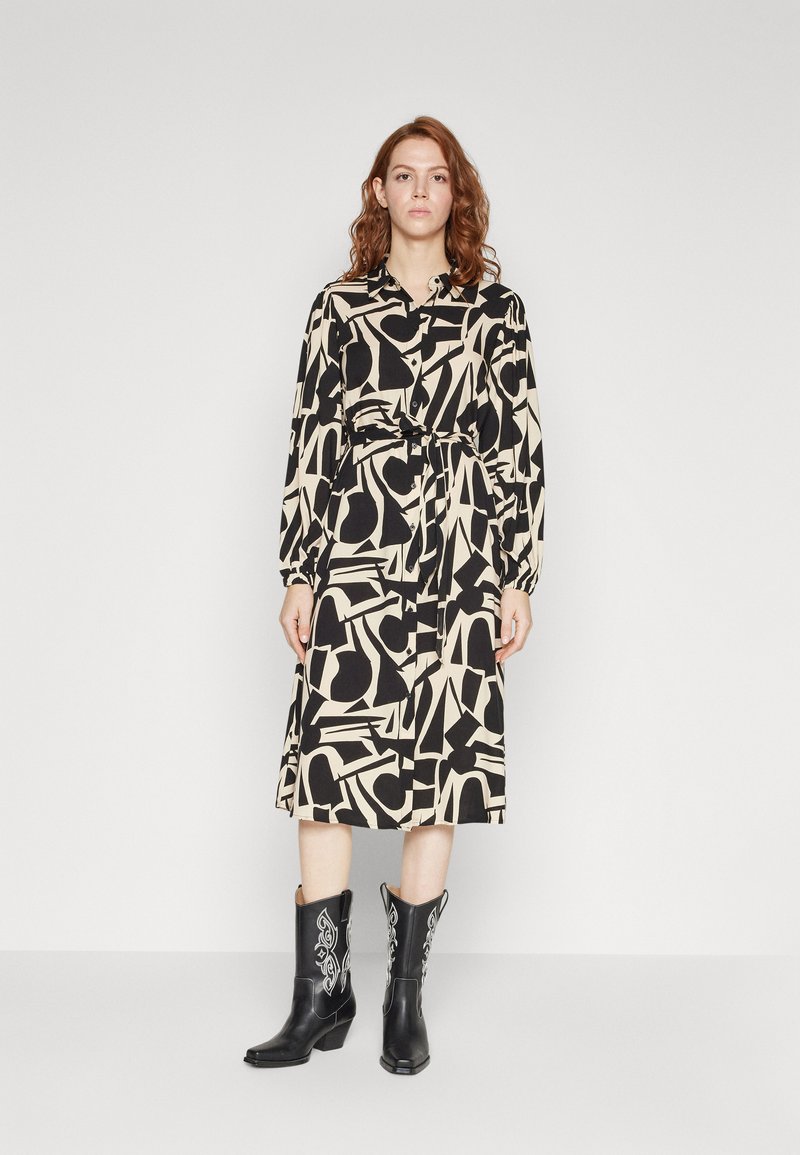 Black and beige dress with abstract patterns, long sleeves, collar, and waist tie. Paired with black cowboy boots featuring white accents.