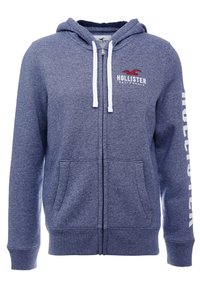 Mörkblå zip-up huvtröja med en röd logotyp och vit text på ärmen, samt två framfickor. Mjuk tyg med en avslappnad design.