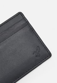 Black leather card holder with visible stitching, three card slots, and a debossed bird design in the bottom corner. Textured surface.