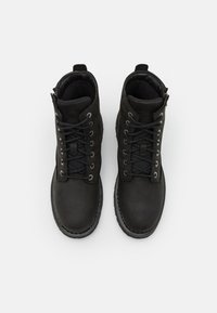 Botas de tobillo de cuero negro con punta redonda, diseño de cordones y ojales plateados. Presentan un cierre lateral y forro de tela texturizada.