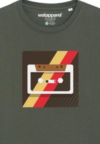 Groene T-shirt met een afbeelding van een cassettebandje met bruine, rode en gele diagonale strepen, en witte knoppen op een donkere achtergrond.