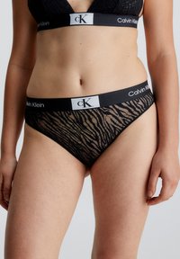 Svart blonde-stringtruse med zebra-stipemønster, med en svart livlinje preget med "Calvin Klein" i hvit tekst.