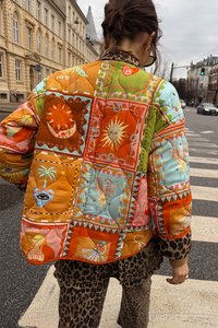 Gequilted jas met een levendig, multikleurig patchworkontwerp dat verschillende patronen en vormen bevat, voornamelijk in oranje, groen en blauw.