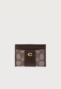 Καφέ δερμάτινο και υφασμάτινο θήκη καρτών με το χαρακτηριστικό μοτίβο "C" και χρυσό έμβλημα με το γράμμα "C" στο κέντρο, σχεδιασμένη για να κρατά κάρτες.