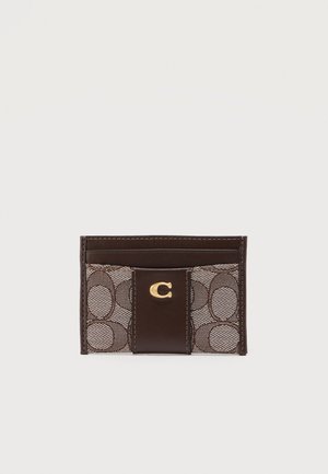 Bruine leren en stoffen kaarthouder met kenmerkend "C" patroon en goudkleurig letter "C" embleem in het midden, ontworpen om kaarten in te bewaren.