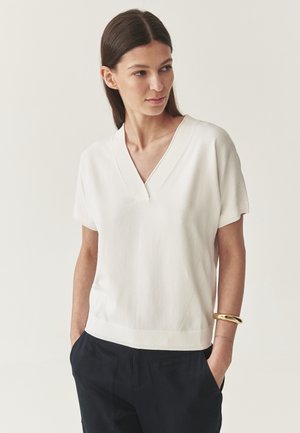 Top bianco a maniche corte con scollatura a V, caratterizzato da cuciture diagonali testurizzate e una vestibilità rilassata. Realizzato in un morbido misto cotone, l'orlo si posiziona sui fianchi.
