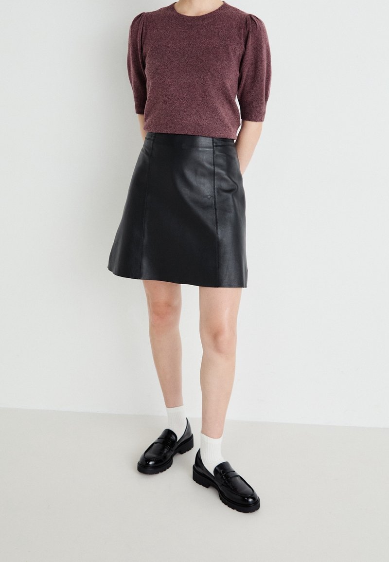 Burgundy short-sleeve sweater with ribbed texture, paired with a black leather A-line skirt and chunky black loafers. White socks visible.