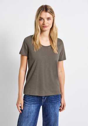 Oliwkowy T-shirt z krótkim rękawem i okrągłym dekoltem, wykonany z miękkiego materiału, zestawiony z niebieskimi dżinsami. Prosty i wygodny fason.