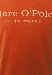 Orange bomulds t-shirt med hvid tekst, der står "Marc O’Polo EST. I STOCKHOLM," med en glat tekstur og rund hals.
