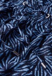 Marina shorts med ett blått lövmönster, med elastisk midja och dragsko med metalldelar. Tillverkade av lättviktsmaterial.