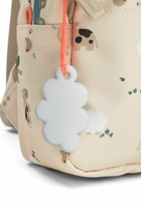 Sac en tissu beige avec des imprimés animaux et une étiquette réfléchissante en forme de fleur suspendue à un cordon orange sur sa poche latérale.