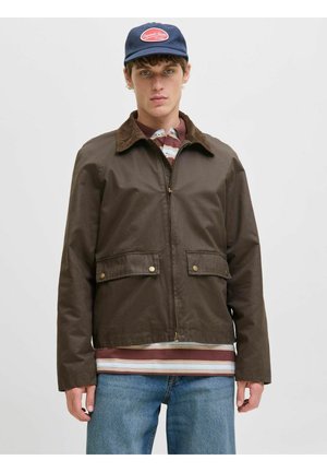 Rjava zip-up jakna s kordurojno ovratnikom, z dvema sprednjima žepoma s pritrdilnimi zapiranji, oblečena čez prugasto srajco, v kombinaciji z modrimi kavbojkami.