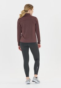 Mørk burgunder langærmet atletisk top med en mock neck, parret med sorte leggings med reflekterende detaljer og grå løbesko.