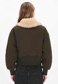 Krótkie bomber jacket w ciemnozielonym kolorze z beżowym, sztucznym kołnierzem z owczej wełny, prążkowanym dołem i mankietami oraz luźnymi rękawami.