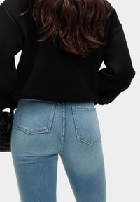 Černá mikina s long sleeves, která je zkombinována se světle modrými, vysokými skinny džíny s dvěma zadními kapsami a jemným vyblednutím.