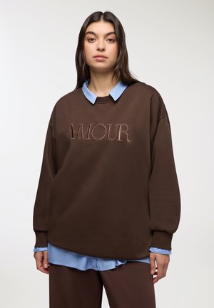 Felpa marrone con "AMOUR" ricamato in marrone chiaro, abbinata a una camicia colletto azzurro chiaro. Il design presenta maniche lunghe e una vestibilità comoda.
