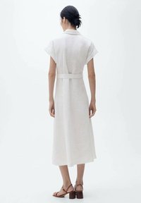 Rochie albă din in cu mâneci scurte, talie marcată, și fustă fluidă de lungime medie. Textură netedă și detalii de design minimaliste.