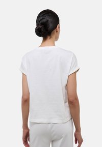 T-shirt en coton blanc avec des manches retroussées, col rond et coupe décontractée, montrant une texture lisse et un design minimaliste vu de l'arrière.