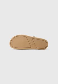 Semelle d'espadrille beige avec une surface texturée et une forme arrondie. Présente un minimum de détails et une base plate en caoutchouc solide pour une meilleure adhérence.