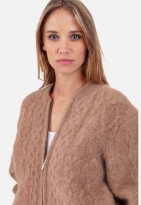 Brauner Cardigan mit strukturierter Oberfläche, Reißverschluss vorne, geripptem Kragen und Zopfmuster. Weiches, flauschiges Material für mehr Wärme und Komfort.