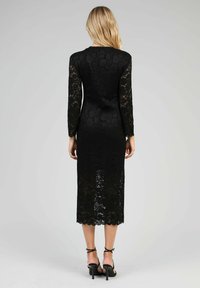 Robe en dentelle noire avec manches longues, longueur mi-mollet et ourlet festonné. Design ajusté avec une couche sous-jacente lisse.