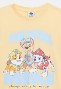Τρία κουτάβια της Paw Patrol με εξοπλισμό διάσωσης κάτω από το κείμενο «PAW PATROL HEROES πάντα έτοιμοι να σώσουν» σε κίτρινο φόντο.