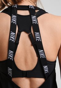 Top sportivo nero con design a trapezio, con spalline regolabili contrassegnate "NIKE" in bianco. Texture liscia con chiusura sicura sul retro.