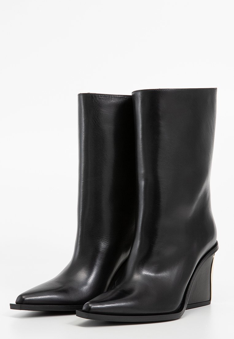 Bottines en cuir noir avec un bout effilé, surface lisse et un talon compensé distinctif. Design minimaliste sans embellissements visibles.