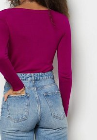 Dopasowana fioletowa bluzka z długim rękawem w połączeniu z jasnoniebieskimi dżinsami z wysokim stanem, wyposażonymi w dwie tylne kieszenie i subtelnym zblaknięciem.