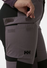 Pantalones exteriores morados y negros con un acabado texturizado, que cuentan con bolsillos de Velcro y un logotipo bordado en el costado.