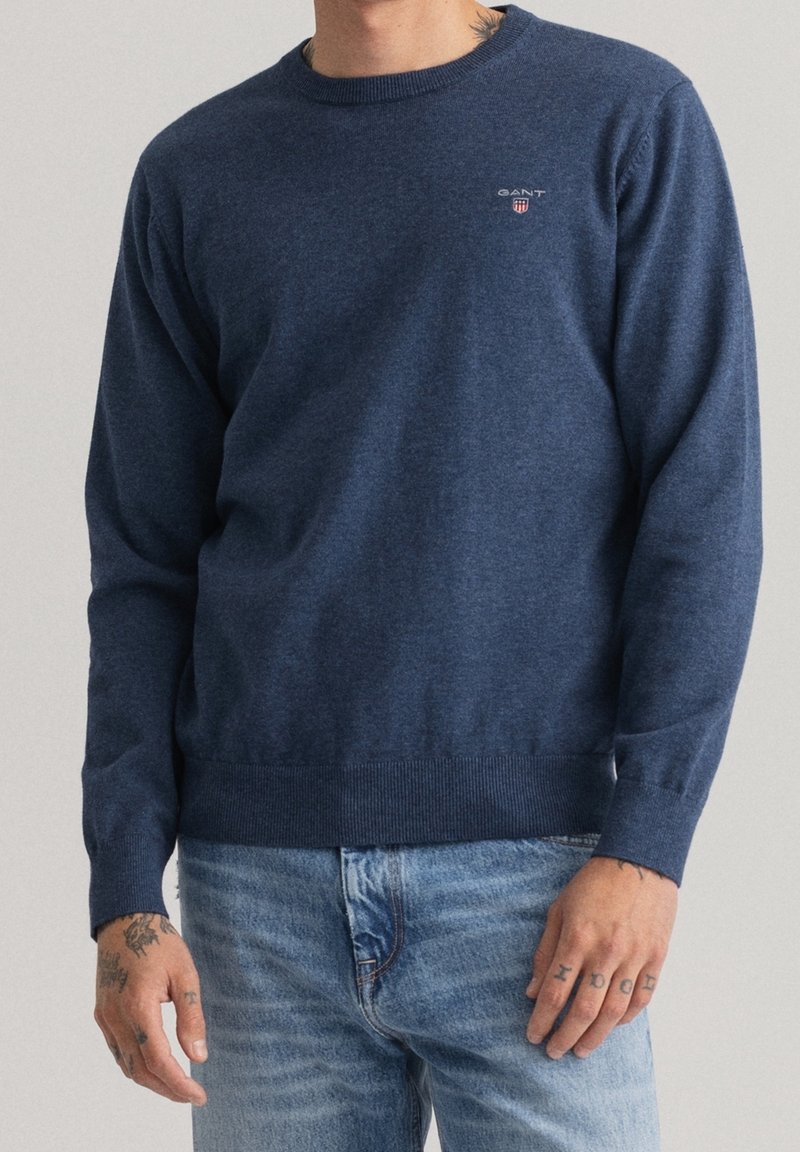 Dunkelblau gestrickter Pullover mit rundem Ausschnitt, geripptem Saum und Bündchen, versehen mit einem kleinen gestickten Logo auf der Brust. Weicher Stoff, lässige Passform.
