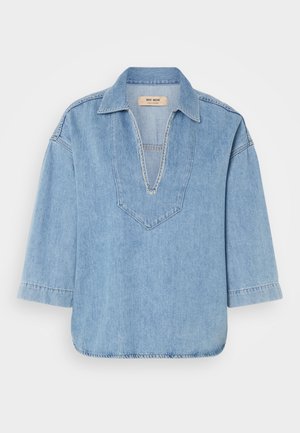 Világoskék denim pulóver ing V nyakkal, rövid ujjakkal és enyhén ívelt hem. A nyakvonal mentén kontrasztos varrás található.