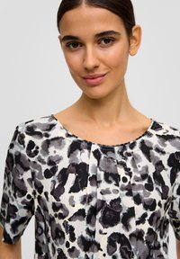 Kurzärmlige Bluse mit einem grauen und schwarzen abstrakten Tierdruck auf hellen Hintergrund, mit gerafftem Ausschnitt und glatter Stofftextur.