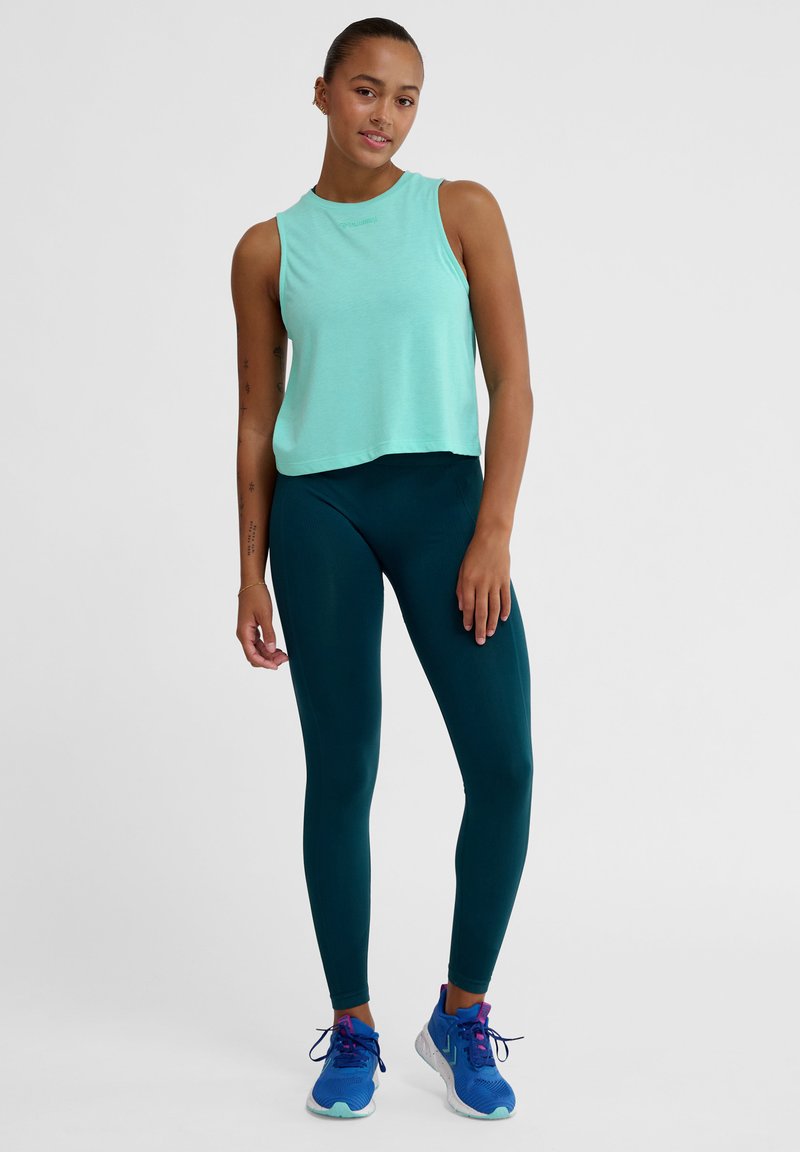 Mintgrünes ärmelloses Crop-Top, kombiniert mit dunkelblauen Leggings und blauen Sportschuhen, aus glattem Stoff und mit tailliertem Design.