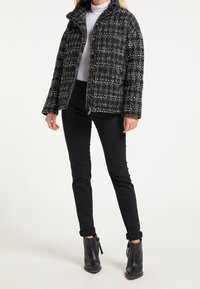 Giacca tweed bianco e nero con chiusura a zip e colletto alto, abbinata a pantaloni neri attillati e stivaletti. 