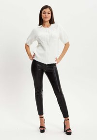 White short-sleeve cardigan with buttons and knitted texture, paired with black fitted leather pants and strappy high-heeled shoes.