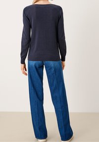 Granatowy sweter dzianinowy z długimi rękawami i ściągaczami, w połączeniu z szerokimi niebieskimi dżinsami. Prosty design bez widocznych wzorów.