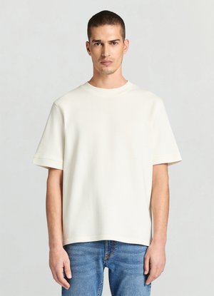 Hellcremefarbenes kurzärmliges T-Shirt aus weichem Stoff, mit Rundhalsausschnitt und lockerem Schnitt, kombiniert mit blauen Jeans.